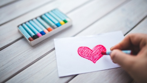 A person drawing a red heart with a crayon.
