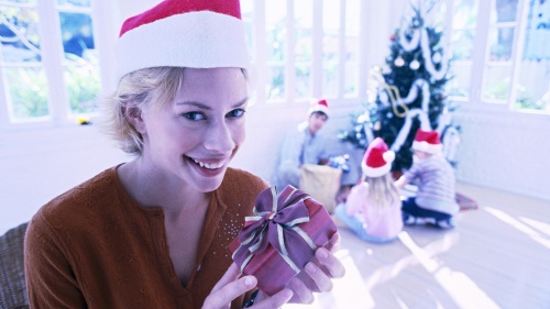 A woman wearing a red Santa hat and holding a gift.