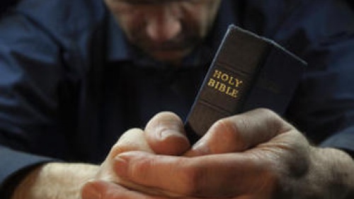 A man praying and holding the Holy Bible.