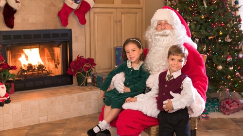 Two children sitting with Santa Claus in front of a Christmas tree.