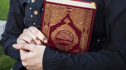 Woman holding a copy of the Quran in her arms.