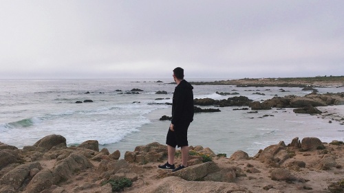 A man walking on a rocky shore of the ocean.