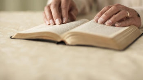 Older hands on top of a Bible.