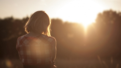 Woman standing in sunset with head down. 