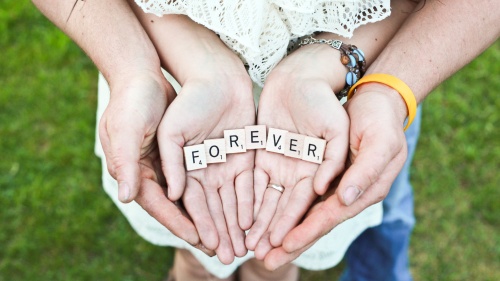 A young married coupling holding in the hands Scrabble letters that spell FOREVER