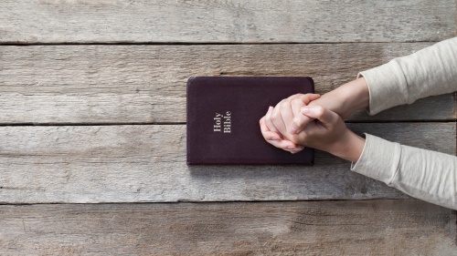 A person with their hands on top of a Bible that is on a table.