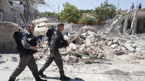 Two soldiers walking in street full of concrete rubble.