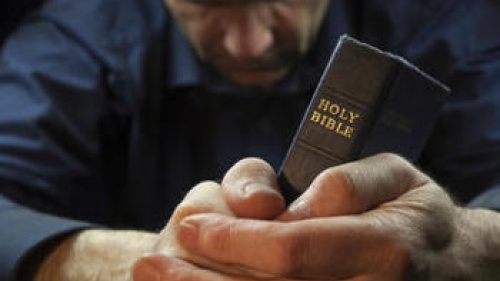 A man praying while holding a Bible.