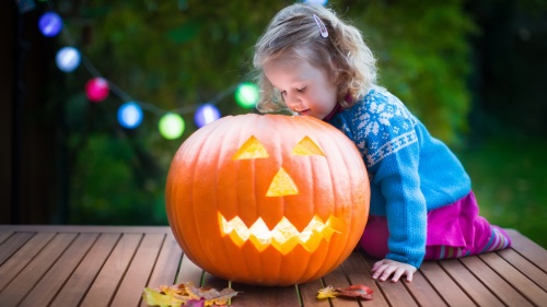 A little girl looking side a carved pumpkin jack o latern