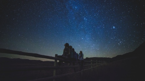 A group of girls sitting on a fence looking up at the stars.