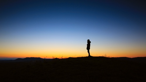 A person standing by thelselves with a colorful sunset.