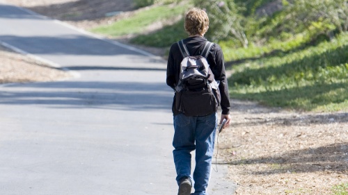 A young boy walking away wearing a backpack.