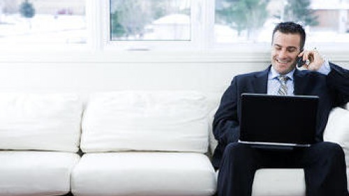 Man sitting on a couch with a laptop and talking on phone.