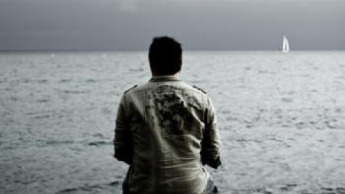 A man sitting on a rock looking at water.