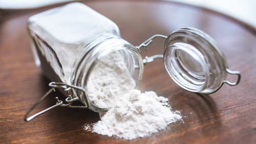 A glass jar of flour on its side with flour spilled out.