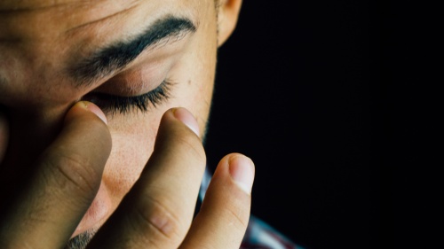 A young man holding his fingers over his eyes.