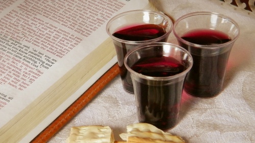 A Bible open to the book of John, small cups of wine and some broken unleavened bread.