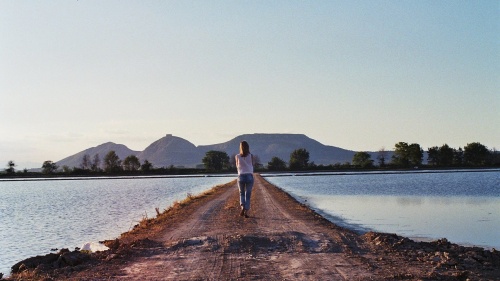 A woman walking on a path between two bodies of water.