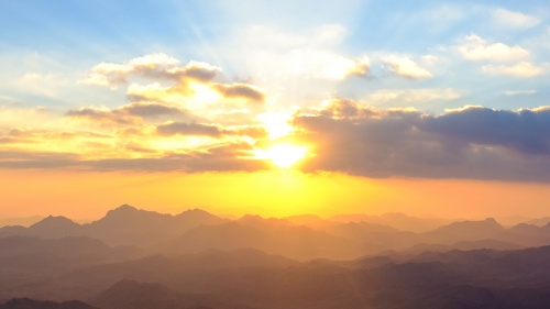 Sunset over a mountain range with clouds in the foreground.