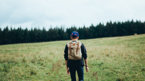 A young man walking up a hill with a backpack.