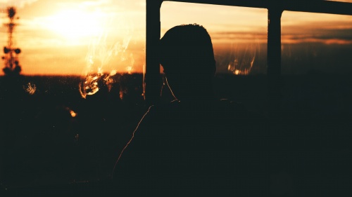 A young man looking out a window with the sun setting.