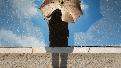 A person holding an umbrella and looking at their shadow.