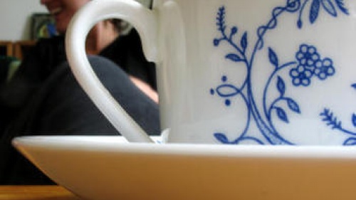 Close up tea cup with woman in background talking.