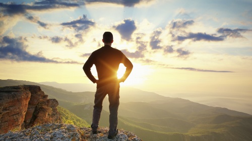 A young man on a cliff looking at the sunset.