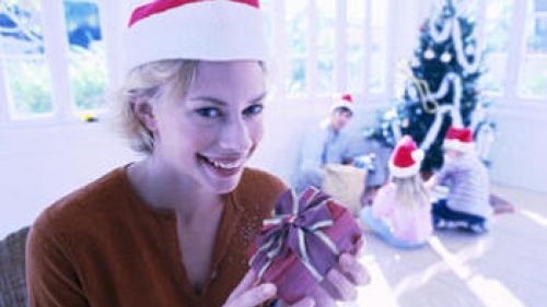 A young woman holding a small present in front of Christmas tree.