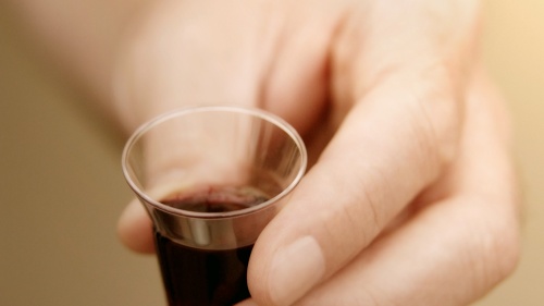 A man holding a small clear cup of wine.