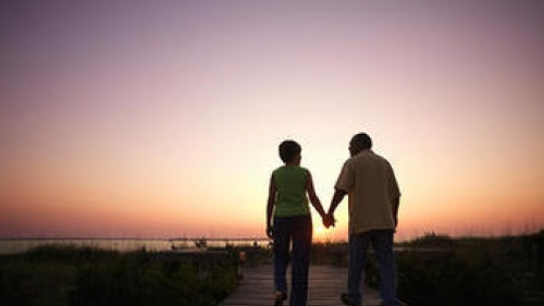 An older couple walking on a board walk while sun is setting.