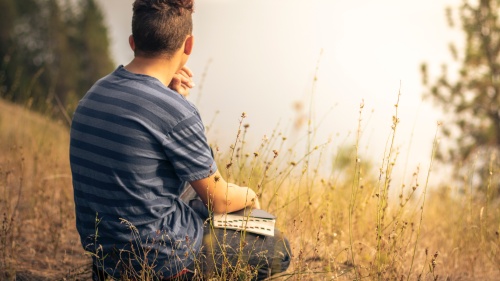 a man sitting outdoors in a field with an open Bible in his lap