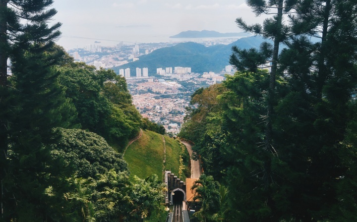 a road cutting through a green landscape towards a foggy cityscape