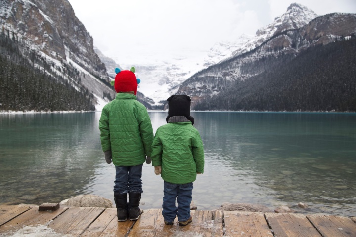 Two young boys look out over the water surrounded by mountains.