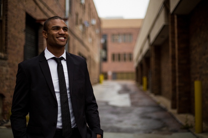 a man wearing a suit and tie standing with a road and buildings in the background