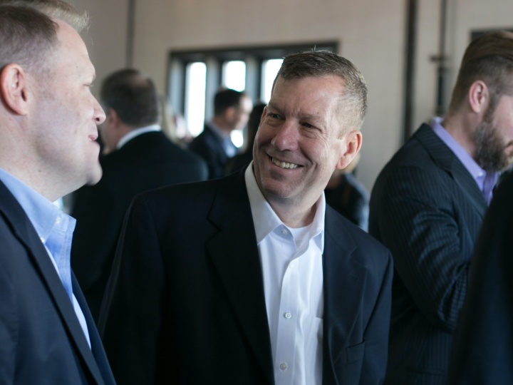 two men wearing suits having a conversation in a room with other people in the background