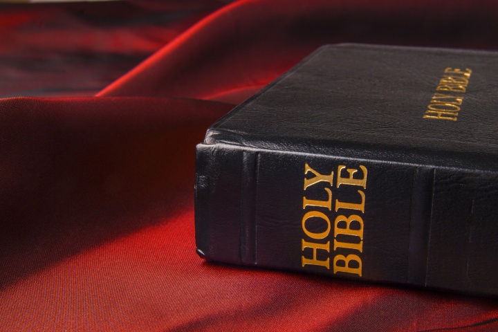 A Holy Bible laying on a table with a red table cloth.