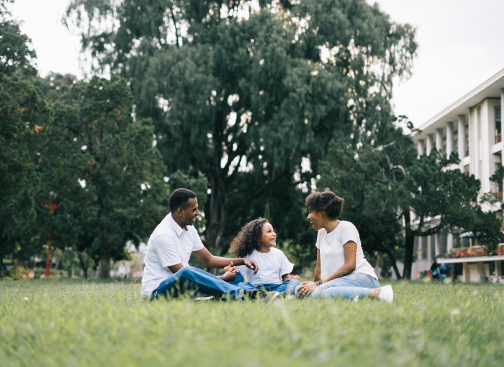 a family of three sitting outdoors in the grass