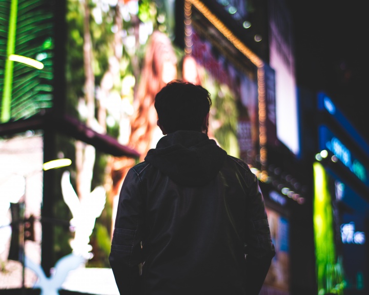 A man walking in a big city with lit billboards.