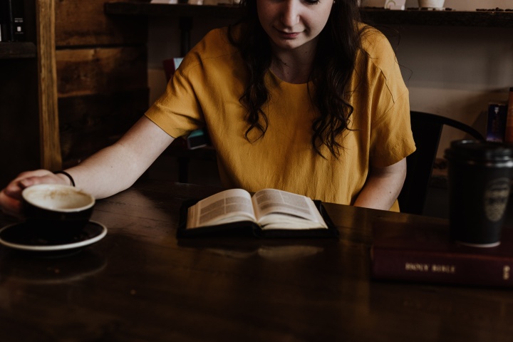 a woman sitting at a table with an open Bible and a coffee mug