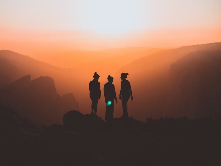 the silhouettes of three women against a backdrop of mountains at sunset.