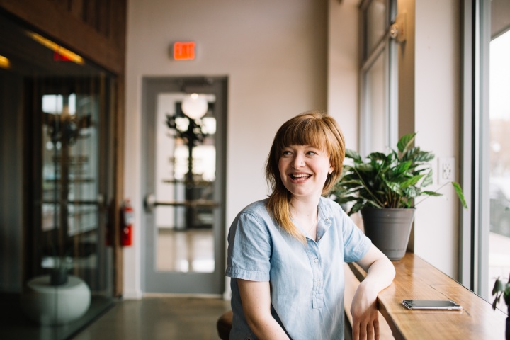 a woman indoors smiles as she sits up to a wooden table