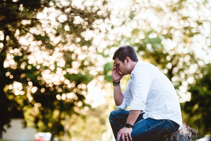 a man sits outside with his head in his hand