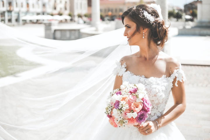 a bride holding a bouquet of flowers with her veil blowing in the breeze