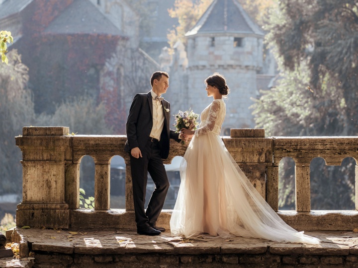 a groom and bride standing against a balcony with historic buildings in the background