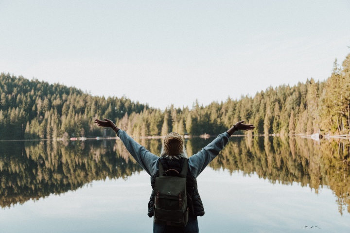 a woman with her arms raised in a joyful gesture facing a lake surrounded by trees