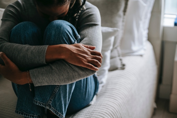 a woman sitting on a bed with her arms wrapped around her knees and her head down