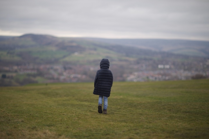 Child in black jacket walking on grass field during daytime.