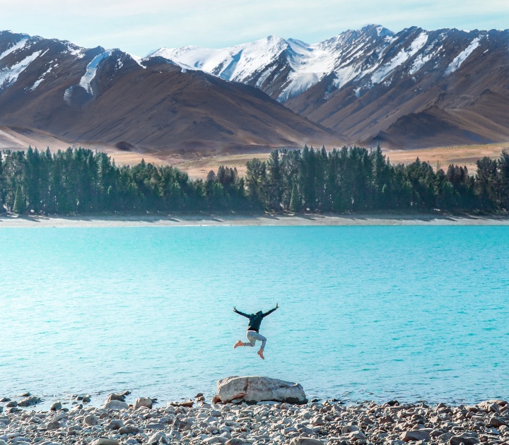 a person jumping in midair above a lake against a mountain backdrop