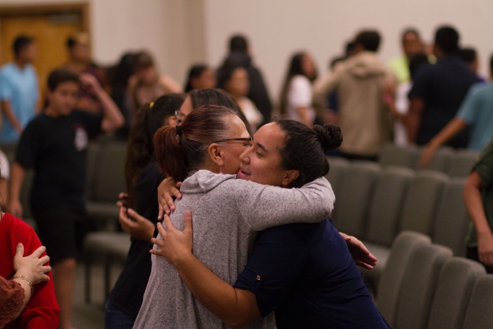 two women hugging in the midst of a room full of people